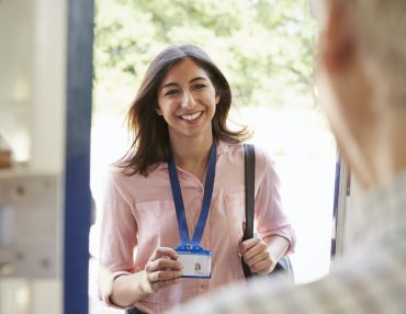 Senior man opening front door to young woman showing ID card